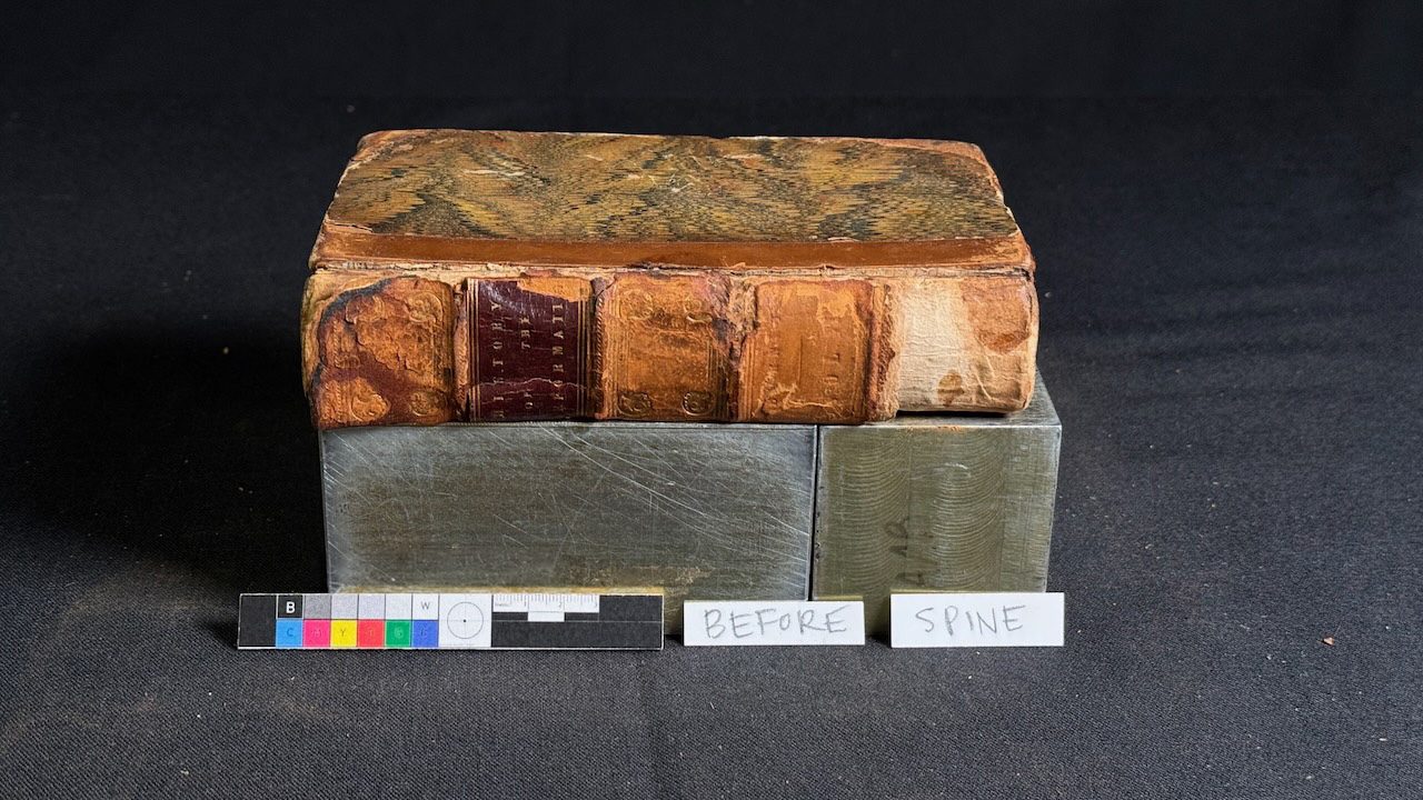 Worn leather book with damaged spine photographed before repair